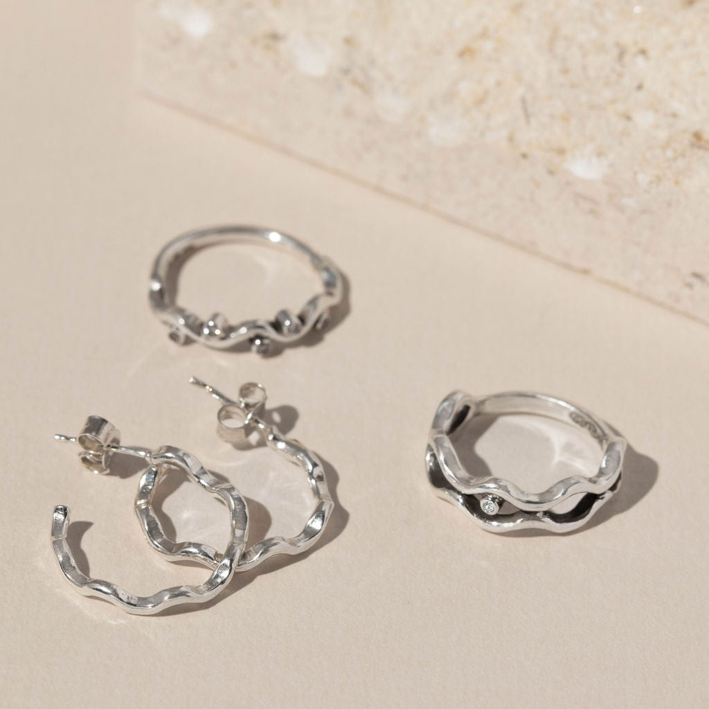Rockpool Jewellery Ocean Collection featuring sterling silver hoop earrings and two organic wave-inspired silver rings, photographed on neutral background