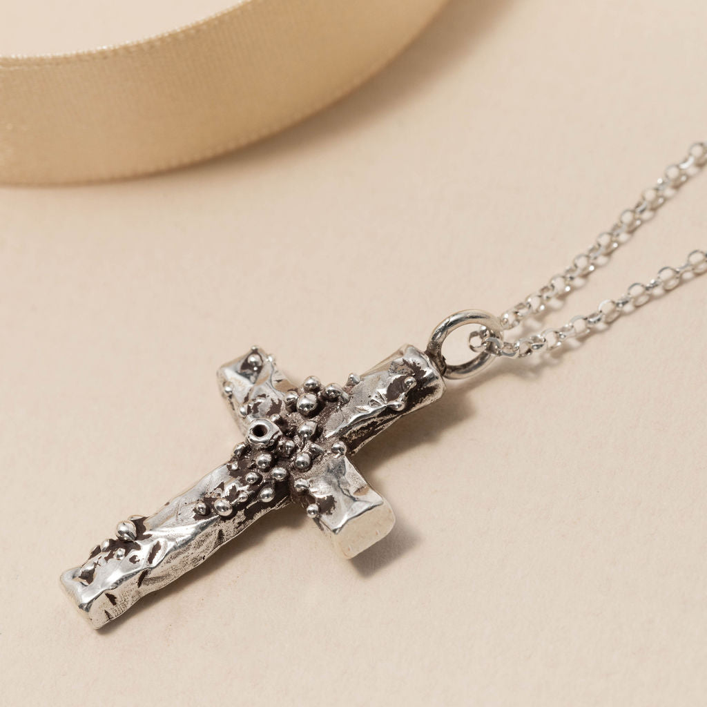 Sterling silver barnacle cross pendant necklace with handcrafted coastal texture, laid against ribbon backdrop, designed by Rockpool Jewellery