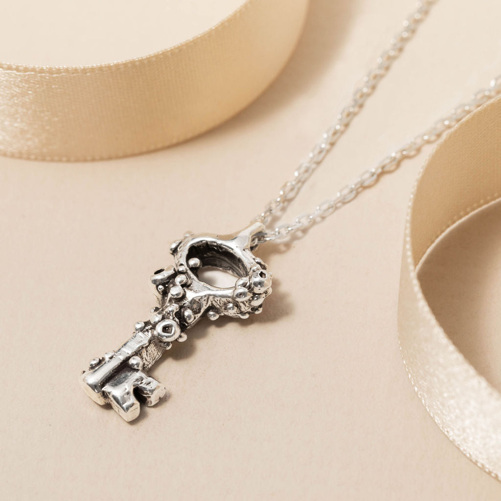 Sterling silver barnacle key pendant necklace with ocean-inspired design, handcrafted in the UK and displayed on cream ribbon background