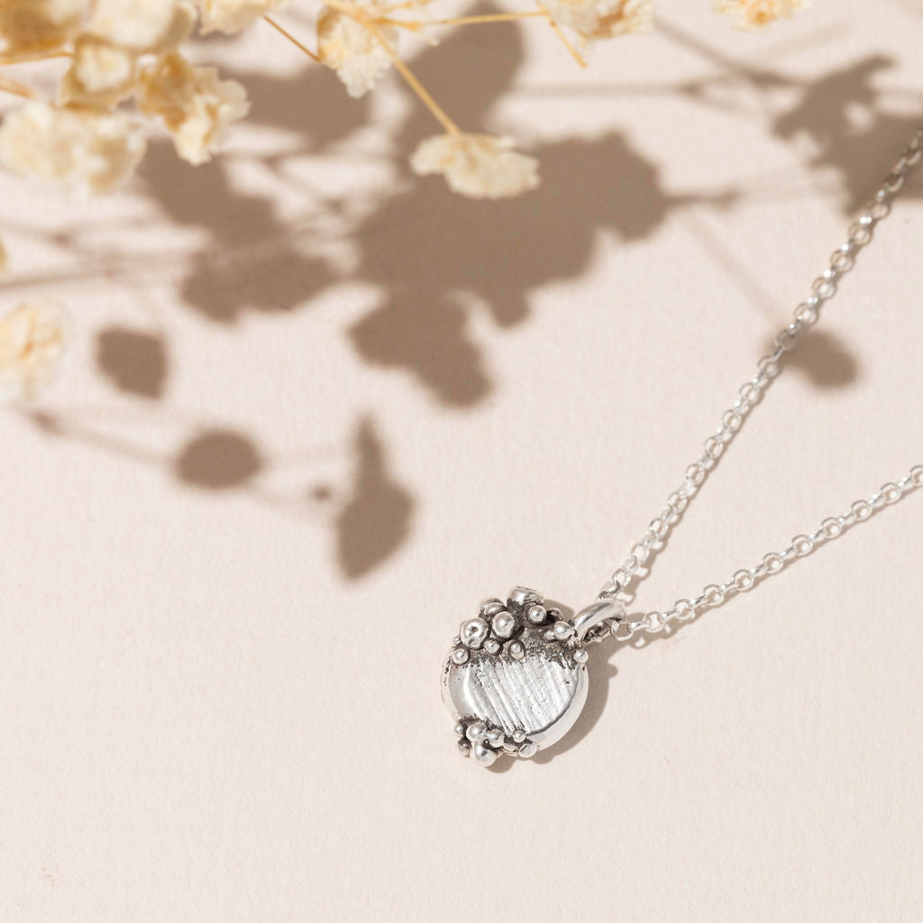 Sterling silver barnacle pendant necklace with round ocean-inspired design, handcrafted in the UK by Rockpool Jewellery and styled with dried florals