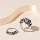Two silver rings with barnacle design, one standing on the ring band and one laid flat on a cream background