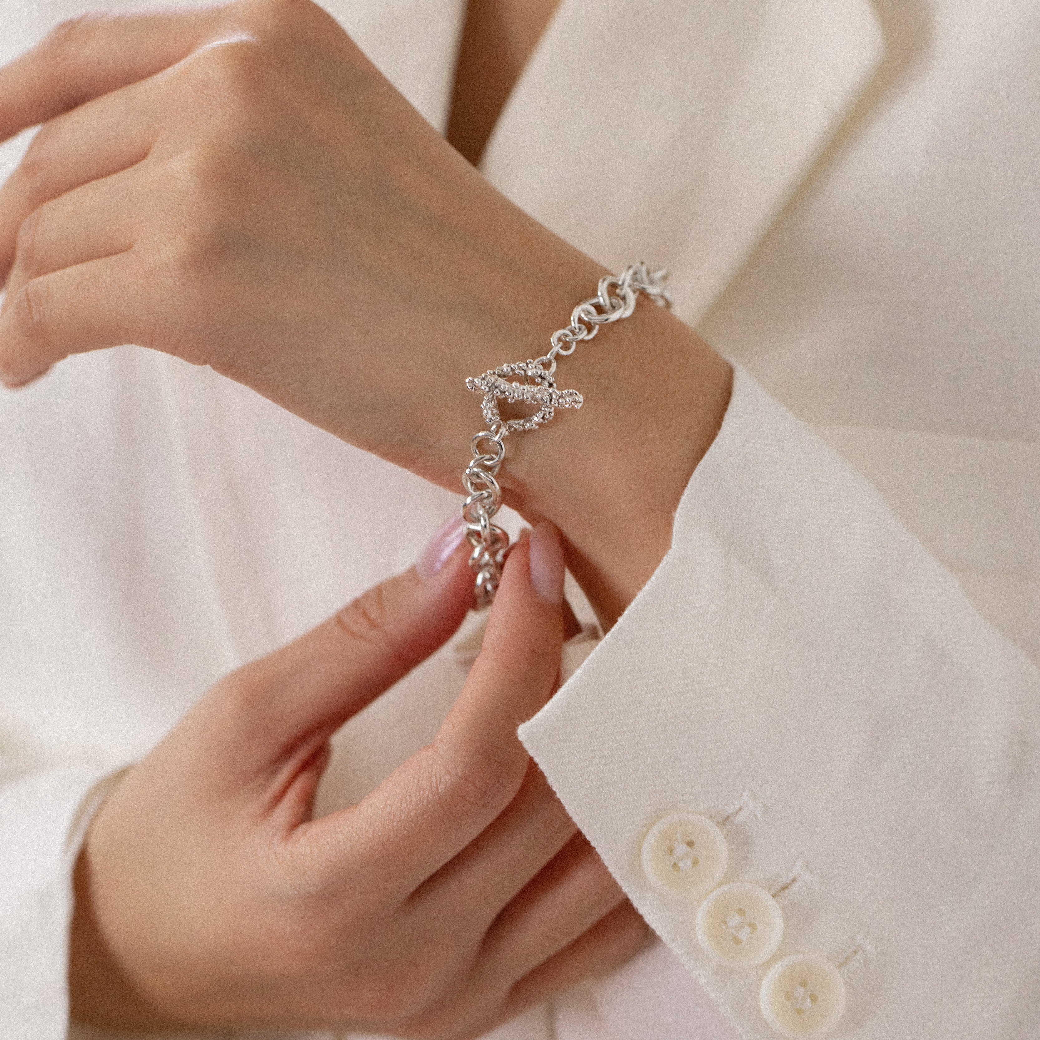 T bar bracelet with granulated clasp shown on models wrist, model wearing white jacket