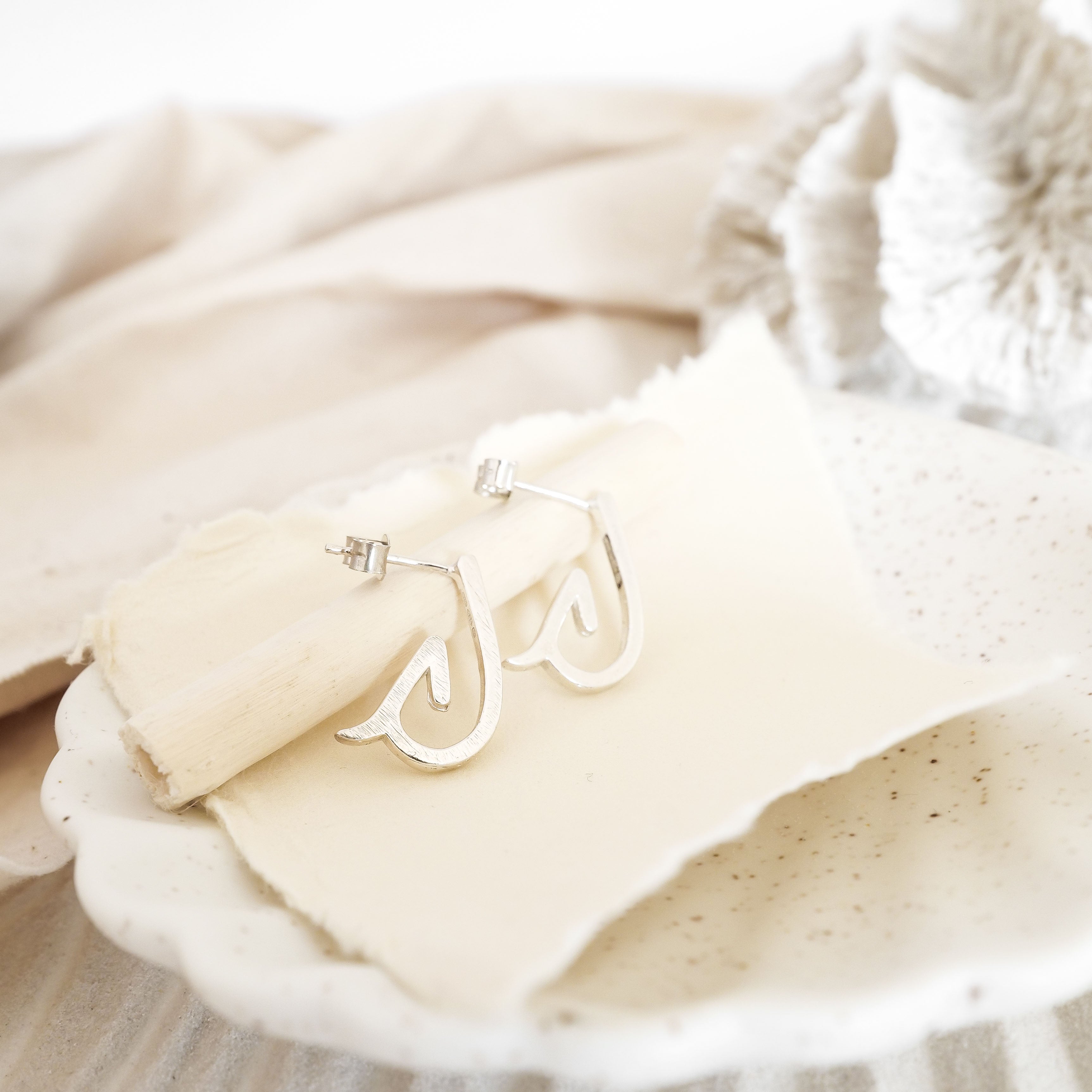 Fishhook shaped earrings on cream fabric
