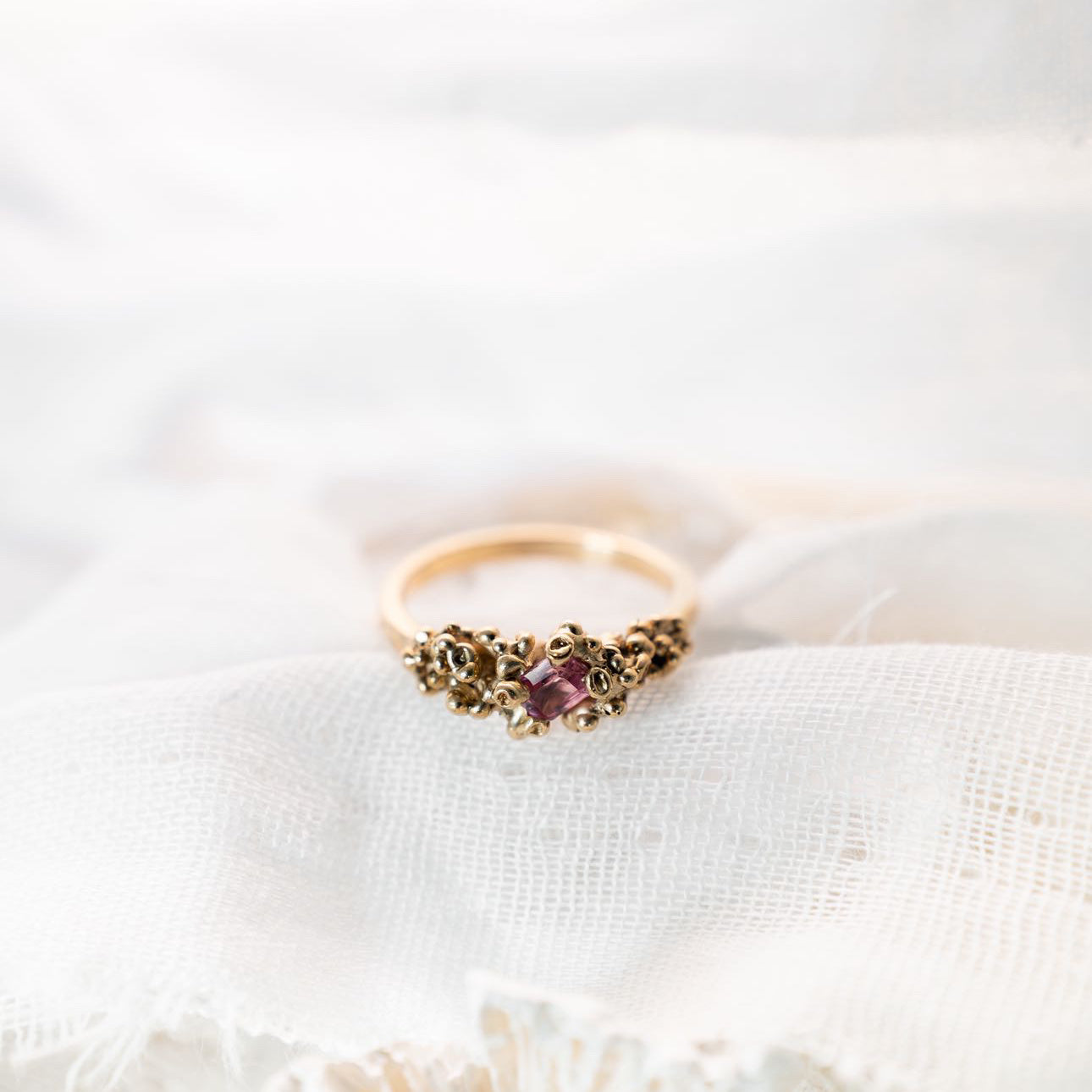 Gold ring with pink stone on white fabric