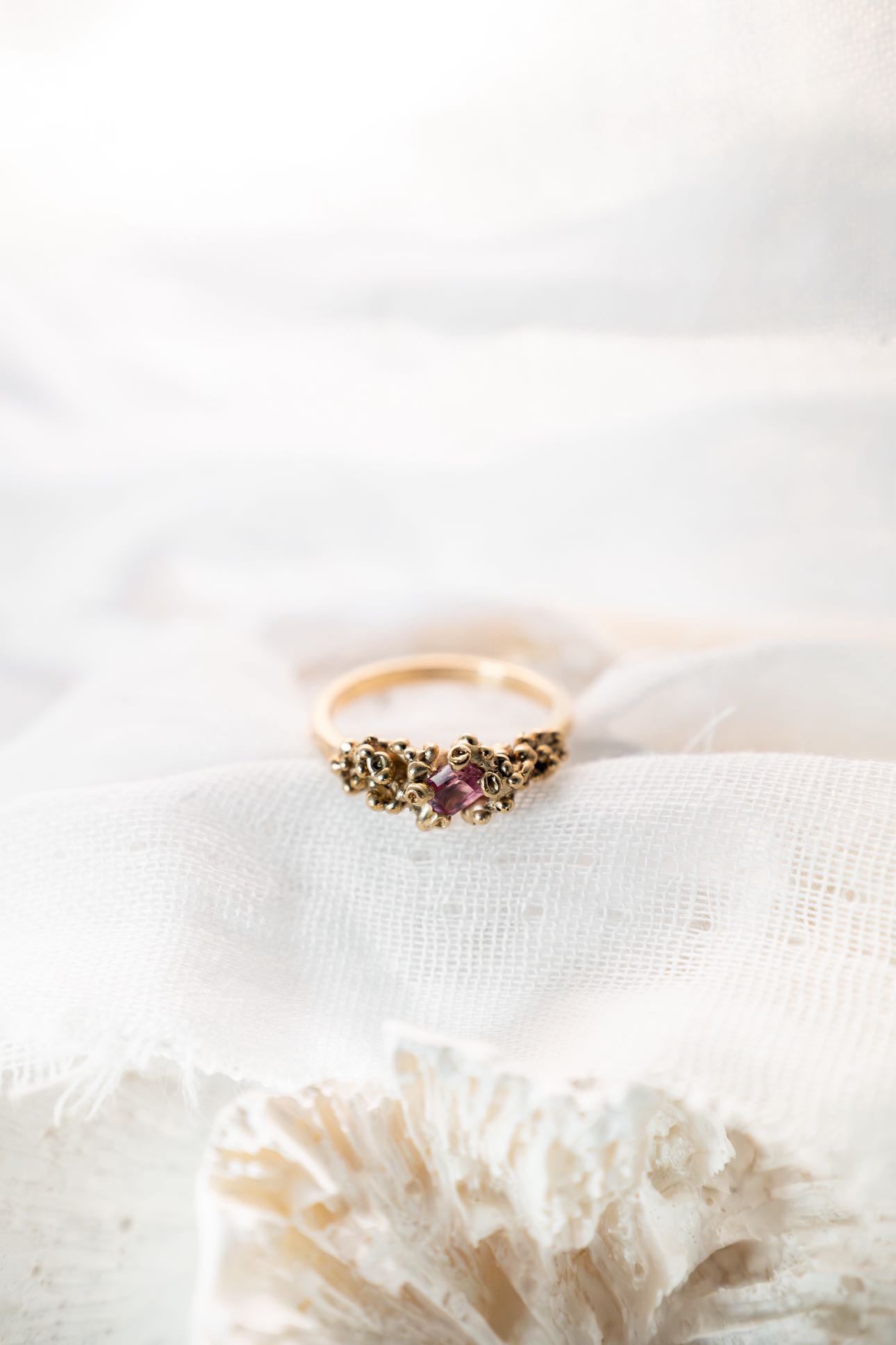 Gold ring with pink stone on white fabric
