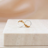 A pair of minimalist gold and silver hoop earrings with small gold rockpool design, displayed on a light beige stone block against a soft beige background.