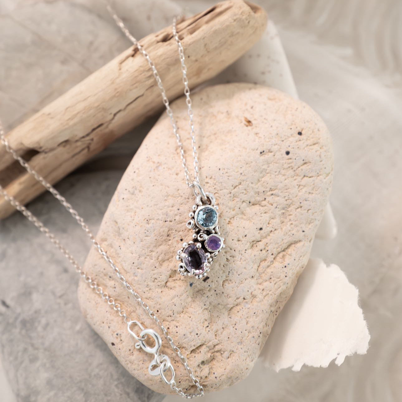 Necklace with a pendant on a stone with driftwood and fabric in the background