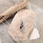 Necklace with a pendant on a stone with driftwood and fabric in the background