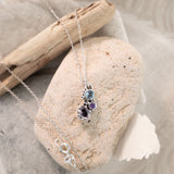 Necklace with a pendant on a stone with driftwood and fabric in the background