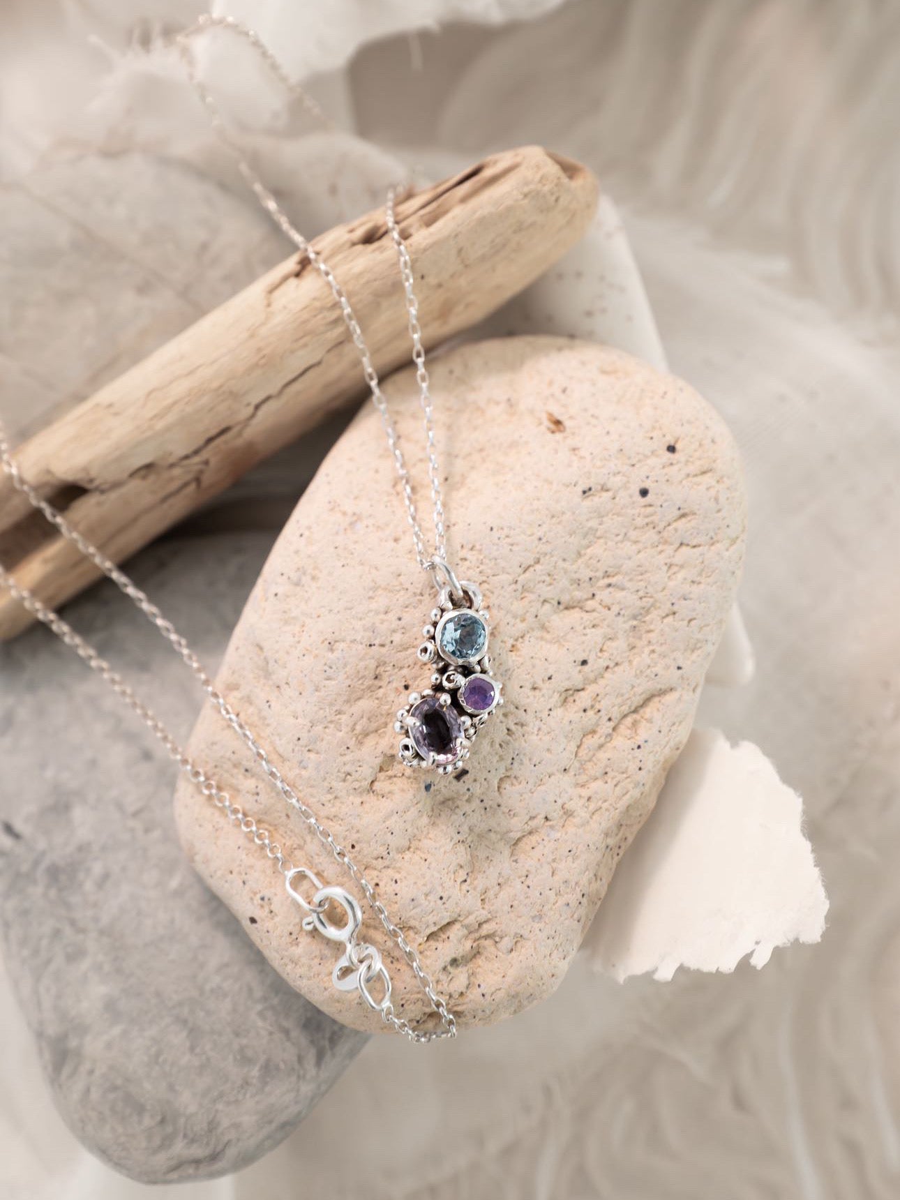 Necklace with a pendant on a stone with driftwood and fabric in the background