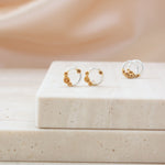 A pair of small hoop earrings with gold-toned spiral details and silver-toned bands, displayed on a light stone block against a soft beige background.