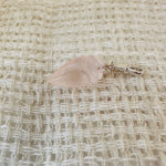 Shell-shaped gemstone charm on a textured beige fabric background