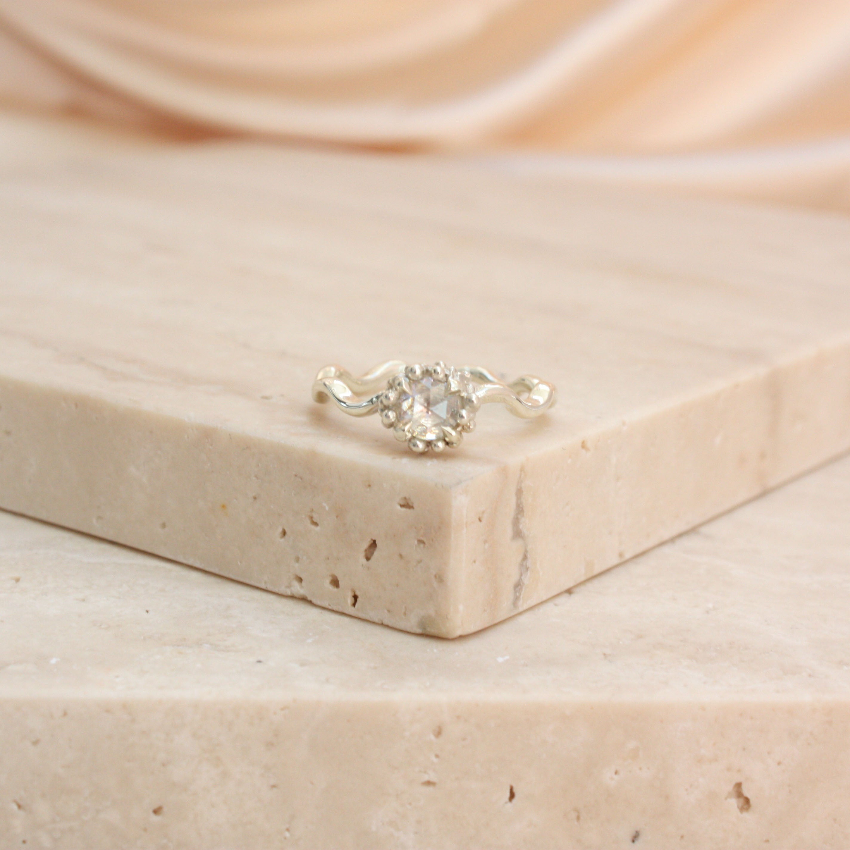 Rose cut diamond solitaire ring with wavey silver coloured gold band on a stone background