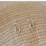 Pair of silver earrings on a textured beige fabric background