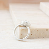 Silver ring lying against stone block with wavy engraved lines on side of setting