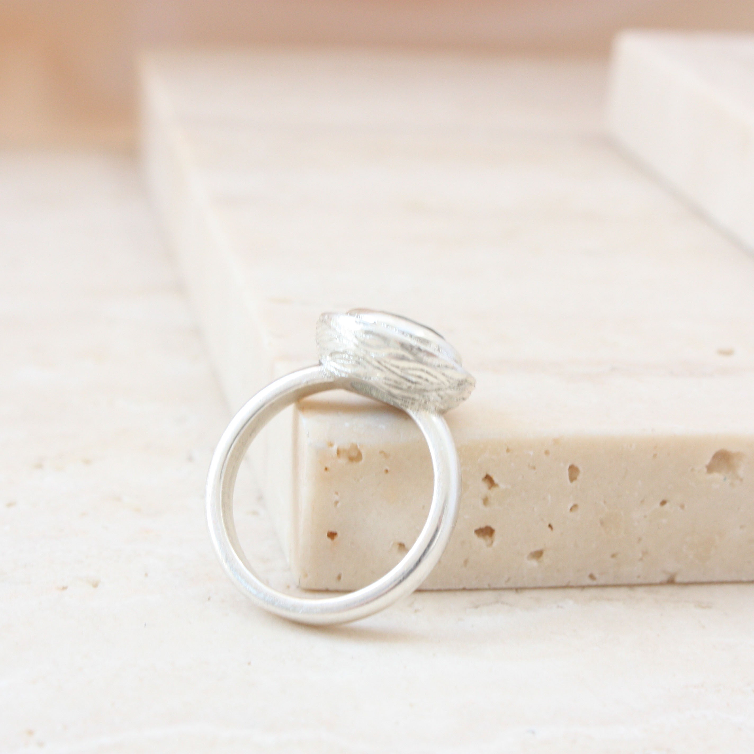 Silver ring lying against stone block with wavy engraved lines on side of setting