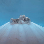 Silver textured earrings on a white surface with a blue background
