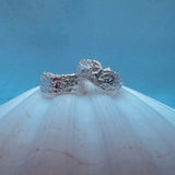 Silver textured earrings on a white surface with a blue background