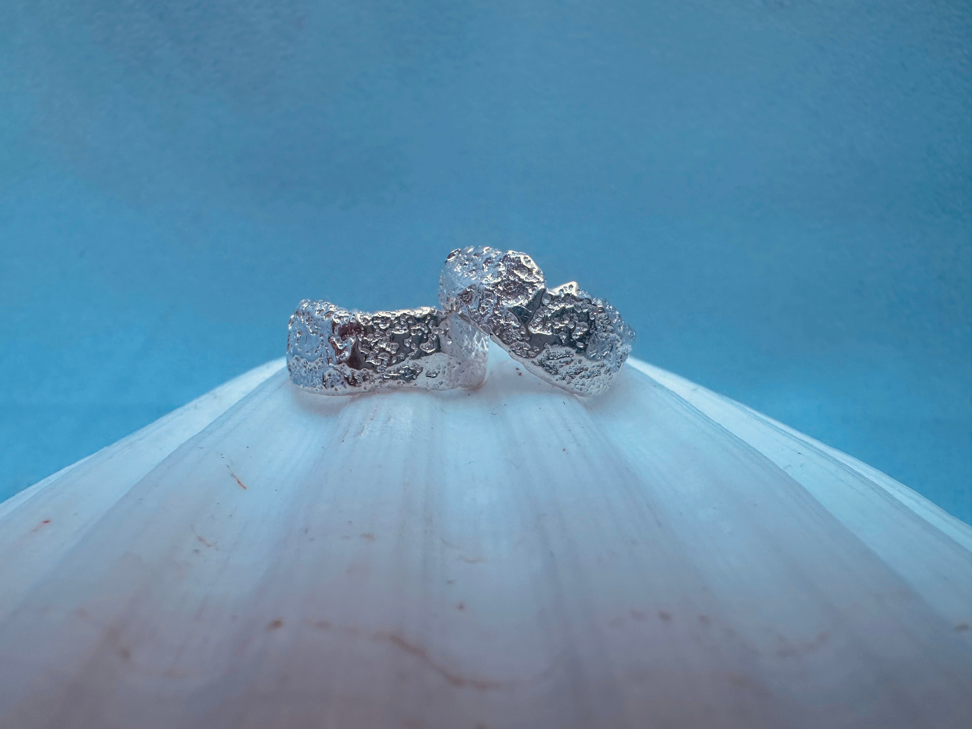 Silver textured earrings on a white surface with a blue background